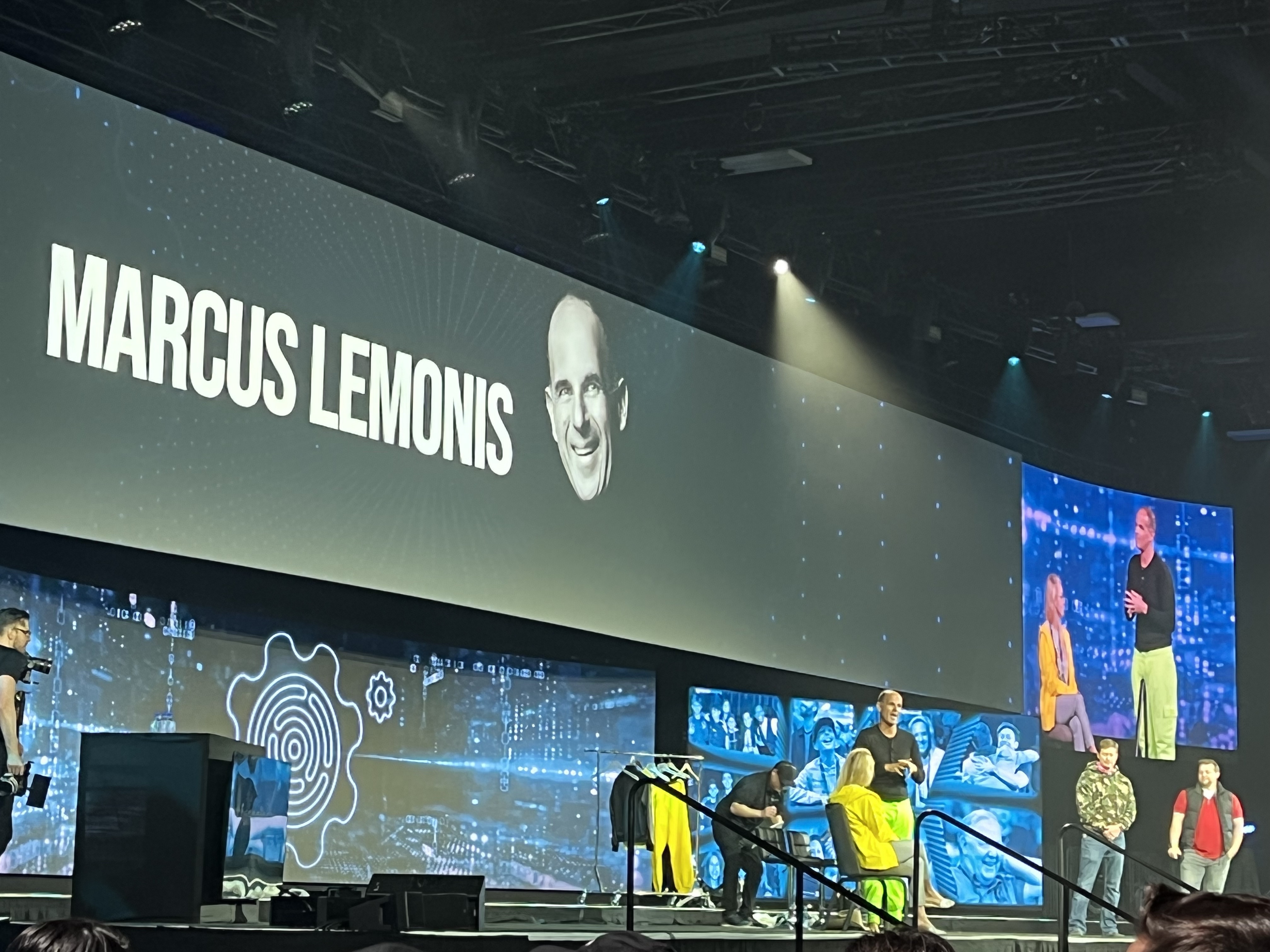Marcus Lemonis on stage with attendees with a screen advertising him